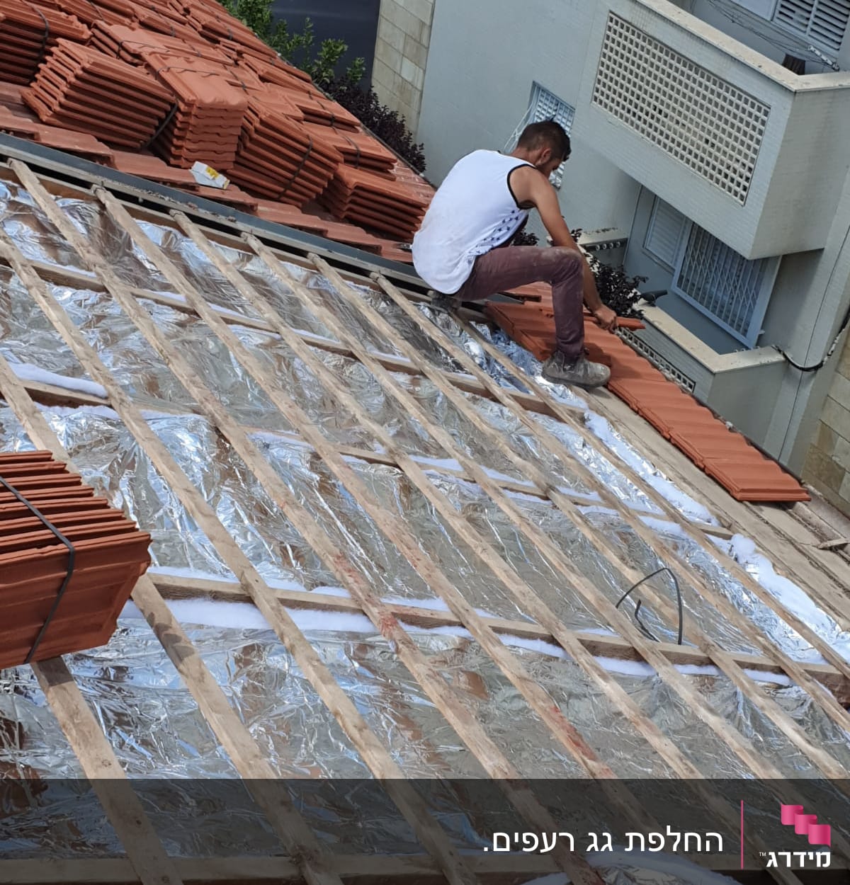 עובד מתקין רעפים על גג עם בידוד מתכתי.